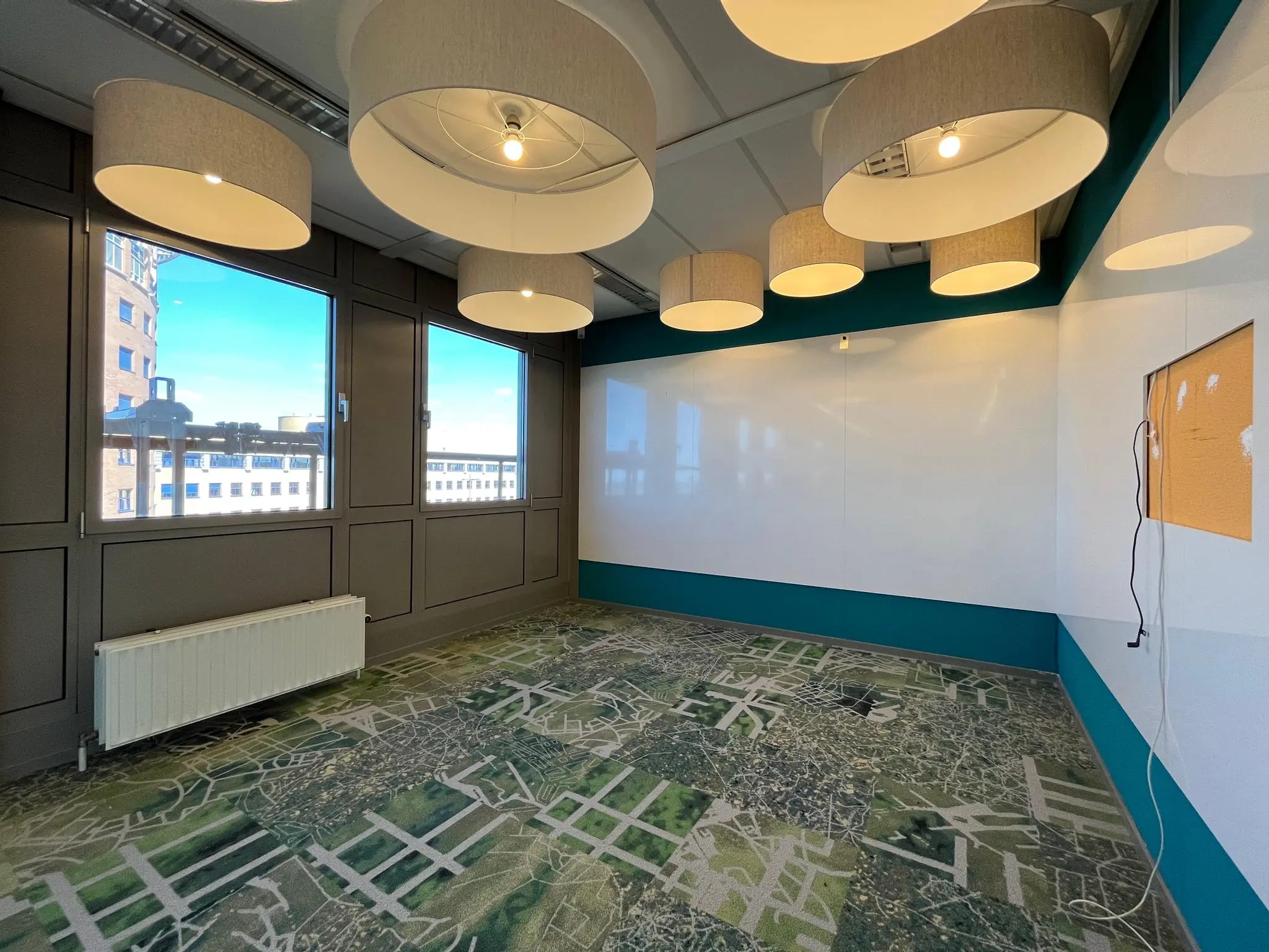 Vergaderruimte aan de Barchman Wuytierslaan met grote ramen, hanglampen, groen tapijt met kaartpatroon en een whiteboardwand.